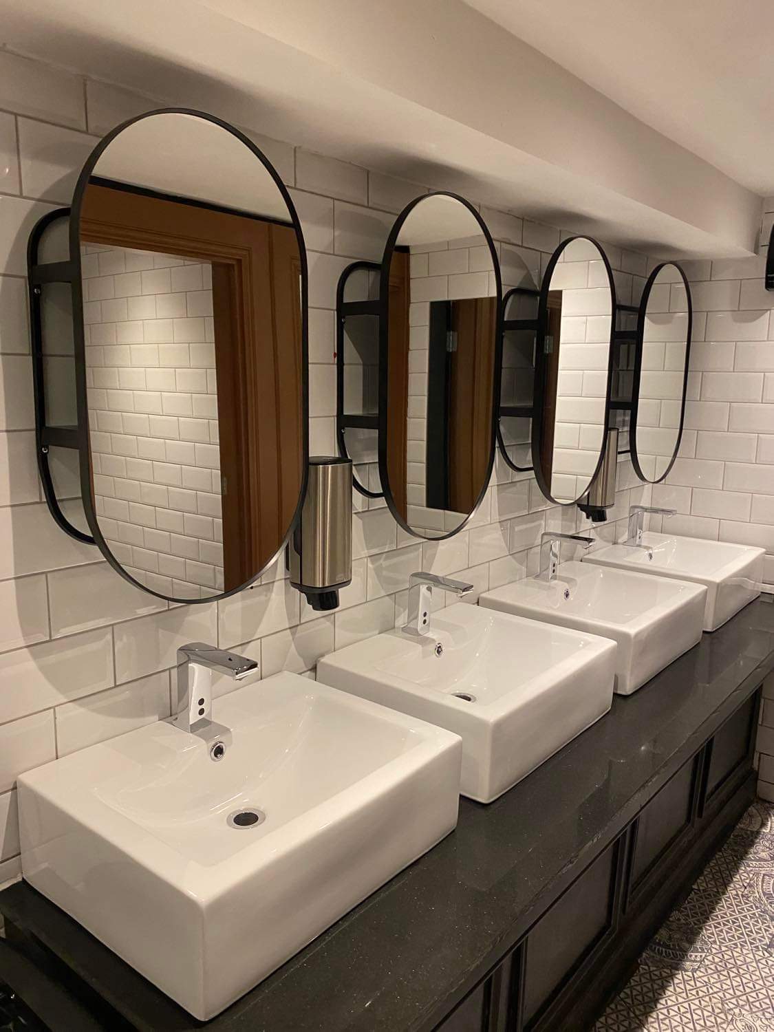 Finished vanity area with white subway tile, round mirrors and vessel sinks