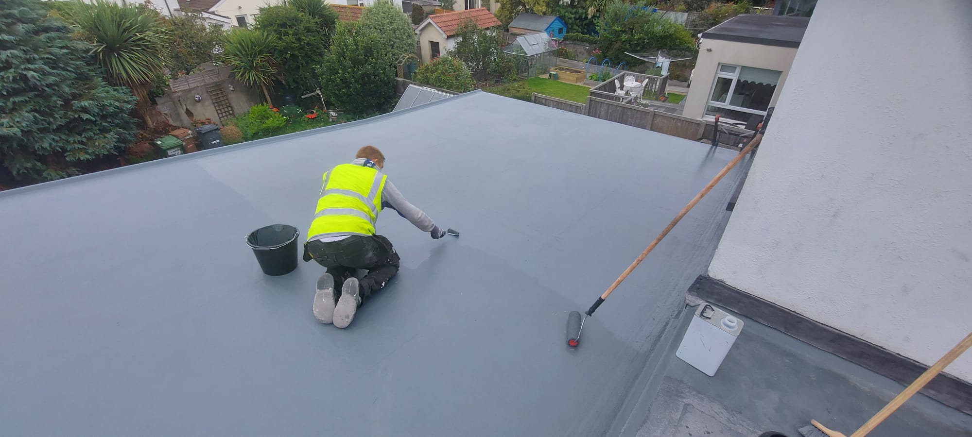 Worker applying the finished grey membrane coating to a flat roof