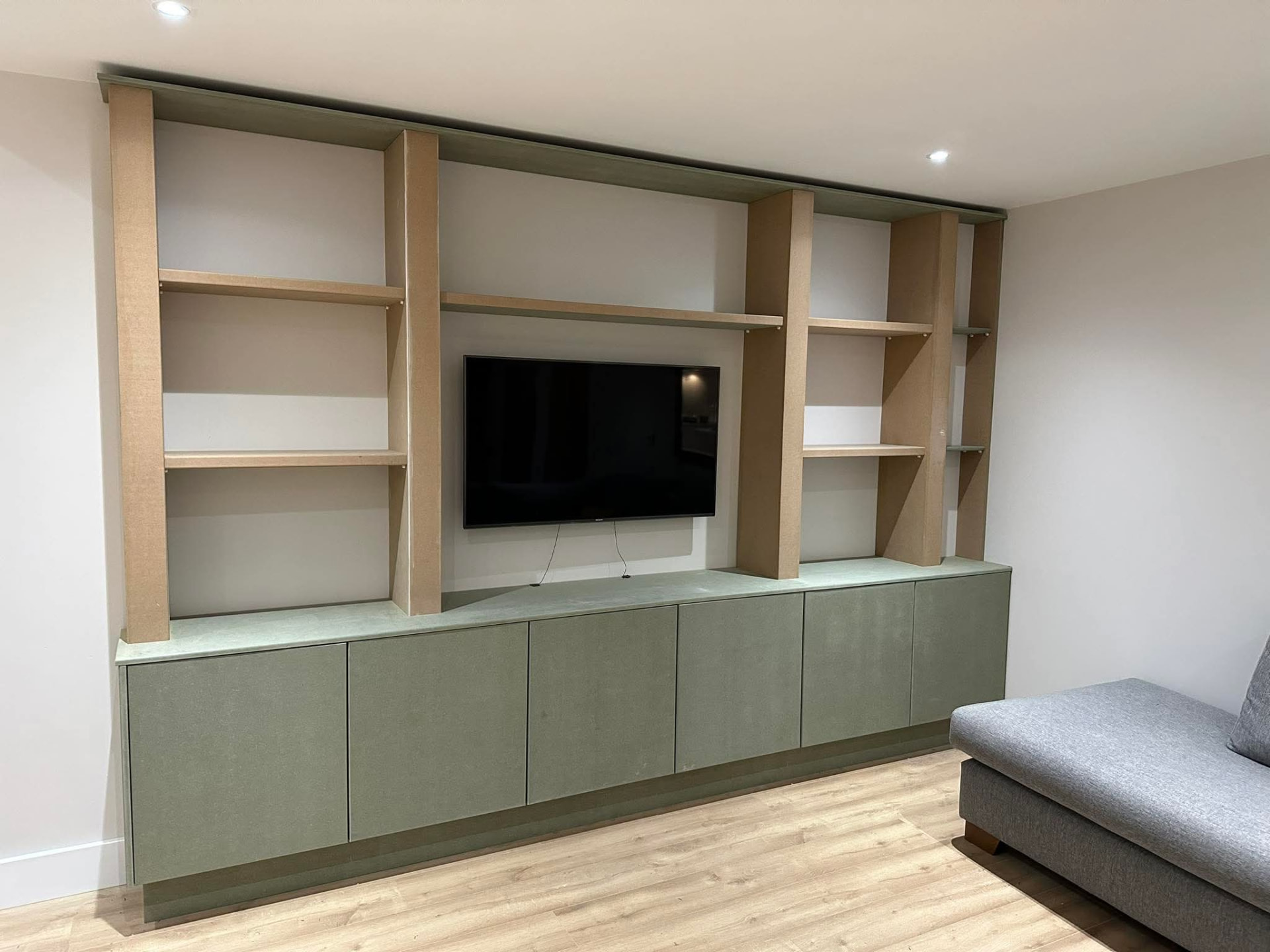 Custom built-in media unit with green cabinetry and timber shelving